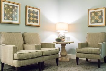 The waiting area of Oak Hills Endodontics. The walls are pale green and softly illuminated by a lamp. There are three armchairs.